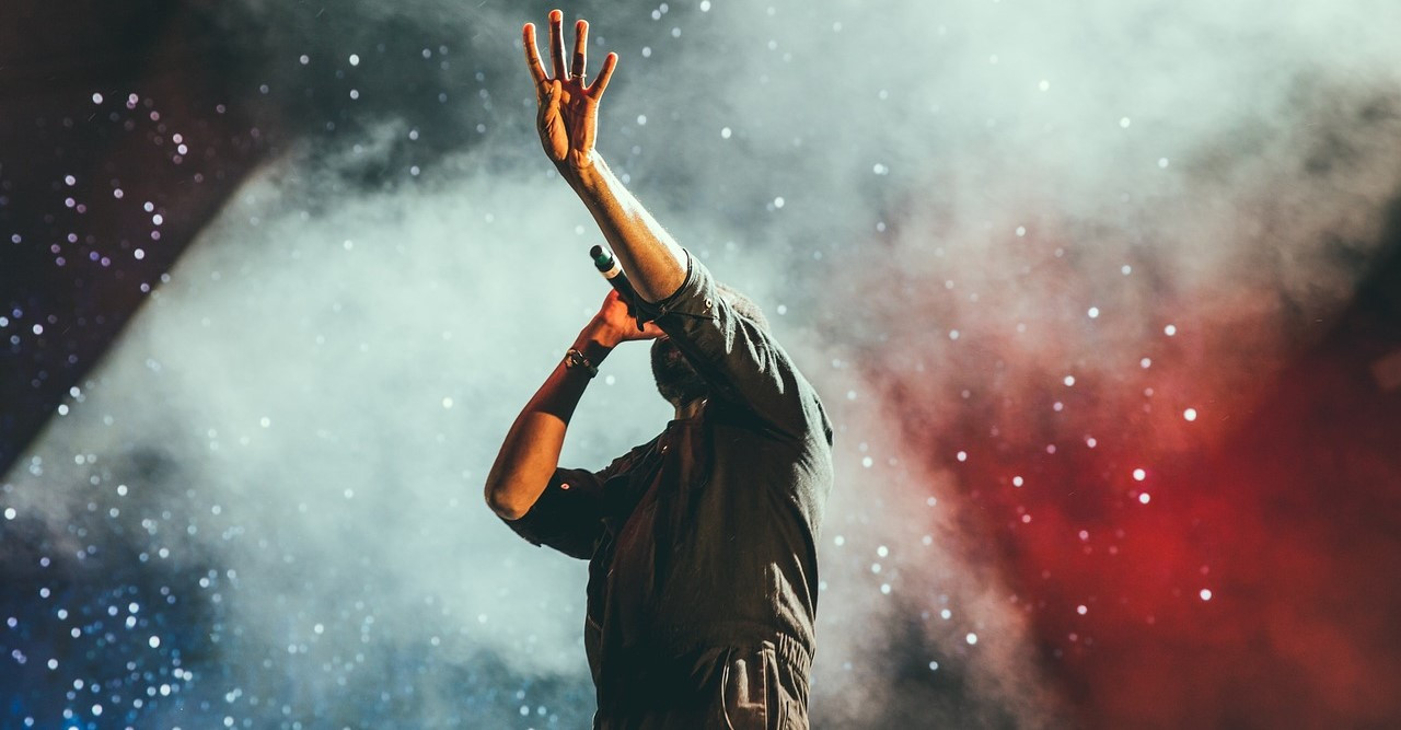 Sänger mit Mikrofon performt auf einer Live-Bühne und hält vier Finger in die Höhe.