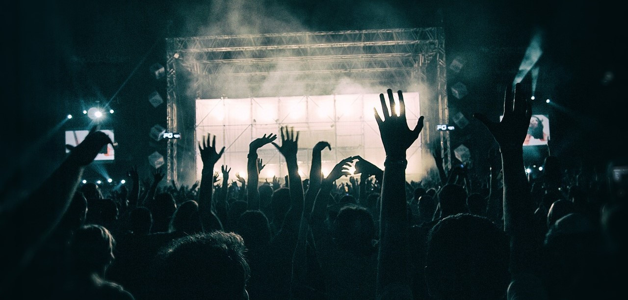 Eine Bühne aus Sicht des Publikums, in schwarzweiß, Publikum hält Hände in die Luft.