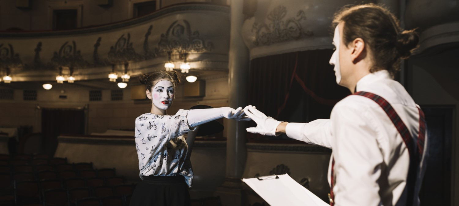Zwei Pantomime-Darsteller reichen sich die Hände auf der Bühne eines alten Theaters.