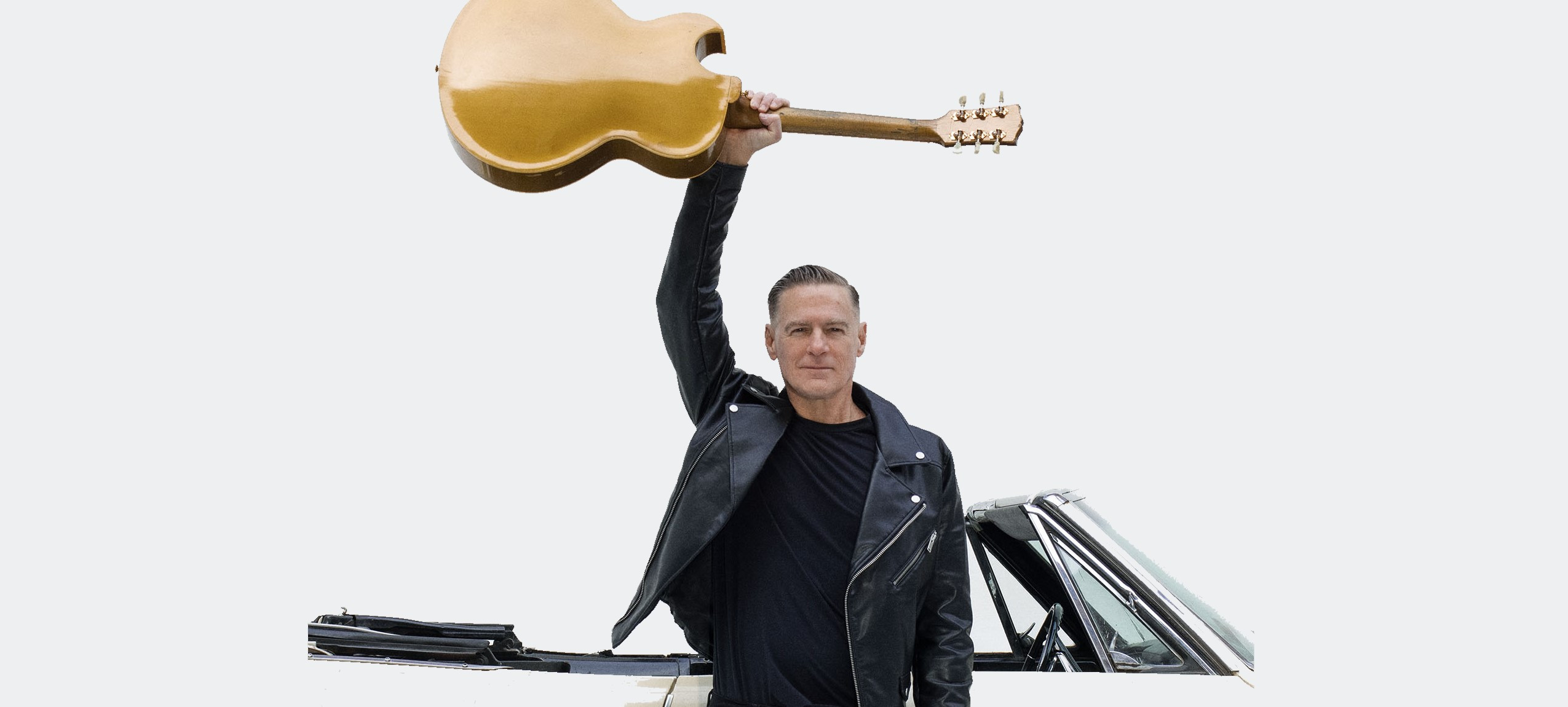Schwarz gekleideter Mann hält beige Gitarre in die Luft. Im Hintergrund ein weißes Auto.